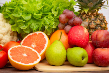 Group vegetables and Fruits Apples, grapes, oranges, and bananas in the wooden basket with carrots, tomatoes, guava, chili, eggplant, and salad on the table.Healthy food concept