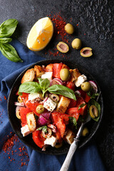 Oriental cuisine. Spicy vegetable salad with spices. Salad of tomatoes, olives, red onions, cheese and basil, croutons on a black cast-iron plate on a black background with red spices. Top view