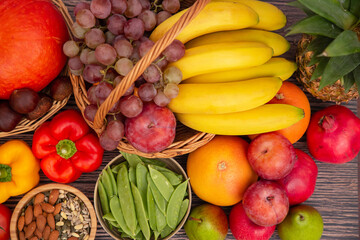 Group vegetables and Fruits Apples, grapes, oranges, and bananas in the wooden basket with carrots, tomatoes, guava, chili, eggplant, and salad on the table.Healthy food concept