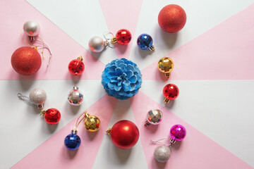 Bright Christmas balls and blue pine cone on multi-colored paper background. Flat lay, free space for text