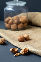 walnuts. unpeeled and peeled walnuts in shells on a black table and in a glass jar. brown nuts with sackcloth on a dark background. copy space. dried walnut and fruit. vertical