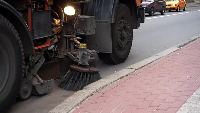 Street sweeper machine cleans town street with brushes. Equipment for cleaning streets and road surfaces. Cleaning Machine brush removing yellow fallen leaves from the autumn street.