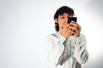 Young Hispanic man with casual clothes on a white background using a cell phone very happy