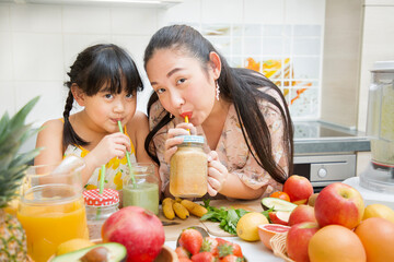 Happy asian family mother and her daughter enjoy prepare freshly squeezed fruits with vegetables for making smoothies for breakfast together in the kitchen.diet and Health concept.