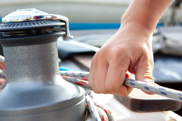 Mans hand pulling winch rope on sailing boat