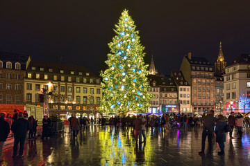 Strasbourg, France. The city's main Christmas tree on Place Kleber. It has traditionally imposing height, at least 30 meters. Tower of Strasbourg Cathedral is visible at the right border of the image.