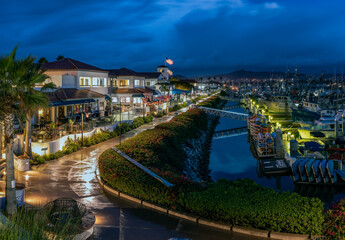 Ventura Harbor Village boardwalk is reflective and wet from the early morning rain with rain clouds reflected in harbor water.