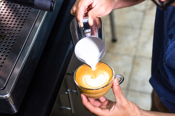 Hand of barista making latte or cappuccino coffee, pouring milk making latte art