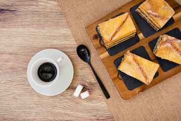 Fototapeta na wymiar Una taza de café, terrones de azúcar y cuchara negra, pasteles de yema de huevo tostadas, sobre fondo rústico y visto desde arriba