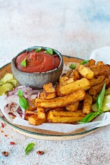 Fried potatoes (deep fried) with herbs and spices, ketchup, pickles and slices of pickled onion on a plate on a light background. Potato food . Baked potatoes with spices and salt.