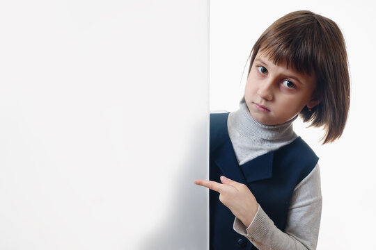 Young cute girl behind white empty banner. She pointing to white wall. Free copyspace area