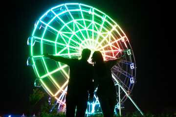 young man and woman romance love in the night in amusement park near ferris wheel