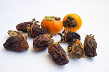 Chocolate persimmon(Hyakume, a variety of chocolate or Zenji-Maru). Large dried fruit whole, brown-yellow with grooves. Ripe orange fruit in the background. Light background.