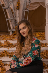 Fototapeta premium A beautiful girl stands leaning against a white railing, an adult with beautiful eyes blonde, in a colored shirt, works on a computer on the background of steps intellect autumn college standing