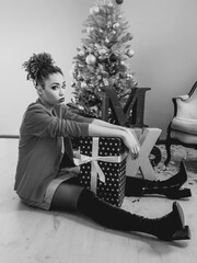 sad afro american woman sitting by the Christmas tree disappointed by  present. Christmas, new year, frustration, happiness, holidays concept