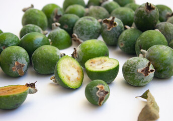 Large fleshy juicy Feijoa berries. Ripe dark green with sepals. A scattering of fruit on a light table. Whole and cut slices.