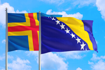 Bosnia Herzegovina and Aland Islands national flag waving in the windy deep blue sky. Diplomacy and international relations concept.