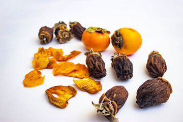 Chocolate persimmon, kinglet. Large dried fruit whole, brown-yellow with grooves. Thin slices, fruit chips. The ripe fruit is orange in color. Light background.