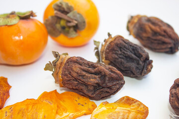 Chocolate persimmon, kinglet. Large dried fruit whole, brown-yellow with grooves. Thin slices, fruit chips. The ripe fruit is orange in color. Light background.