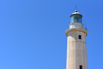 Fototapeta na wymiar Close up of the top of a lighthouse, to the side of the picture, against a blue sky