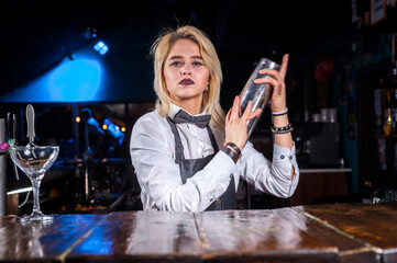 Focused woman mixologist places the finishing touches on a drink while standing near the bar counter in pub