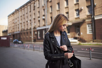 Fototapeta na wymiar A woman in a black jacket walks down the street in the city cropped view