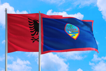 Guam and Albania national flag waving in the windy deep blue sky. Diplomacy and international relations concept.