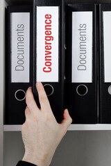 Convergence. File Folder is taking by a hand from office shelf. Red Text is on the label of the...