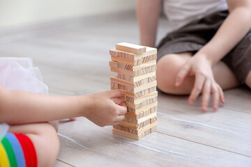 Two Childrens collects a tower of wooden blocks on the floor.