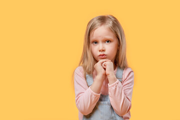 Cute beautiful blonde girl looks at the camera and pray. Yellow isolated background