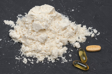 whey isolate protein with fish oil capsules and multivitamin tablet on a black table