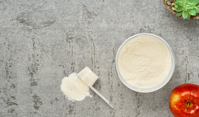 Collagen protein powder in a plastic measuring spoon and jar on a gray stone background, flat lay. Supplemental protein supplementation for body and joint health. On a natural basis. Space for text