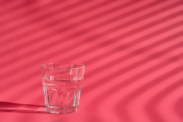 Glass of water on a red paper background bright sunlight, preparation for taking powder collagen. Close-up with copy space for text