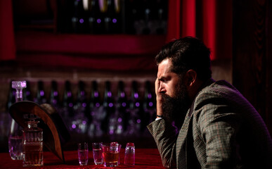 Handsome bearded man looking tired and upset drinking whiskey alone at the bar rubbing his forehead...