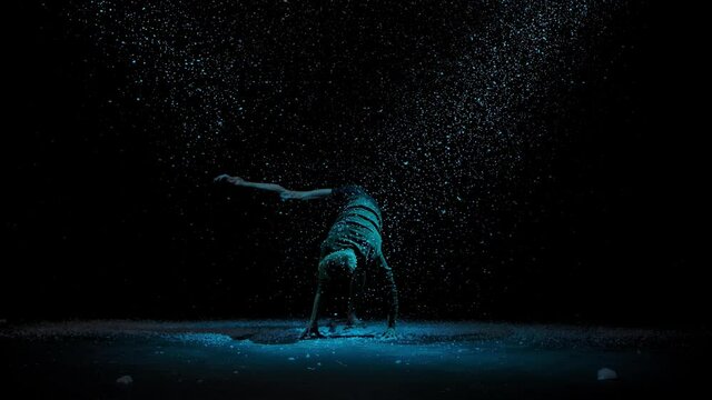 Elements of modern ballet performed by a sensual male dancer. Ballet dancer against the background of falling snow and studio light in slow motion. Silhouette on a black background.