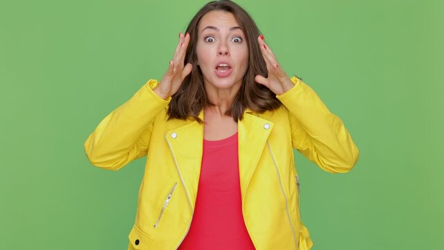 Worried young woman 20s in yellow jacket isolated on green background studio. People lifestyle concept. Clenching fists waiting for special moment keeping fingers crossed say yes doing winner gesture