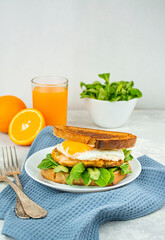 European breakfast, sandwich with fried egg, chicken, herbs and orange juice. Breakfast on a light table, top view. Food background.