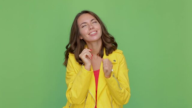Pretty pensive young brunette woman 20s years old in casual yellow leather jacket posing isolated on green background in studio. People lifestyle concept. Looking aside up put hand prop up on chin
