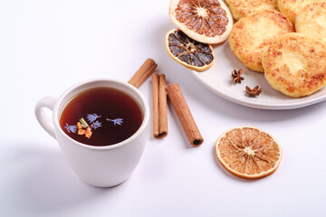 Cottage cheese fritters with hot black aromatic tea, Christmas breakfast mood with anise and cinnamon on white background, angle view