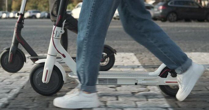 Low section of couple walking with e scooters on city street