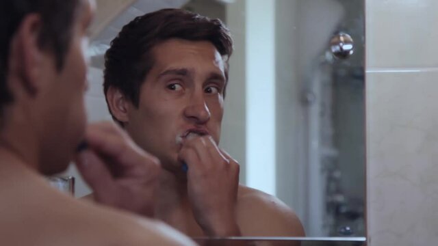 Serious Young man brushing his teeth in front of a bathroom mirror