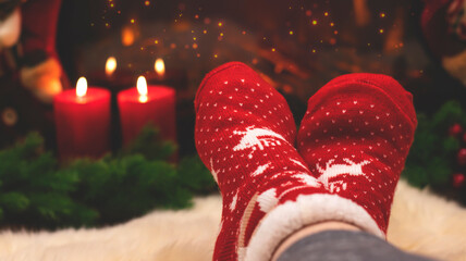Red knitted socks against the background of New Year's decorations and fireplace, Christmas tree garland. Cozy winter evening by the fireplace, blurred background. New Year and Christmas festive backg