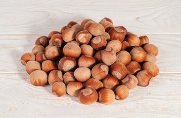 Pile of unpeeled hazelnuts over white wood table. Nuts as an antioxidant and protein source for ketogenic diet and vegetarianism.