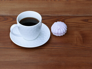 White cup of coffee and pink zefir on the wooden background. Traditional russian sweets like marshmallow.