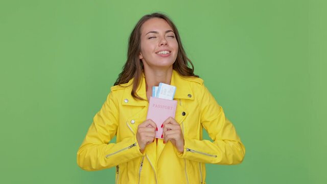 Pensive dreamful young traveler tourist woman 20s years old in casual yellow leather jacket posing isolated on green background in studio. Air flight journey concept. Hold passport tickets looking up