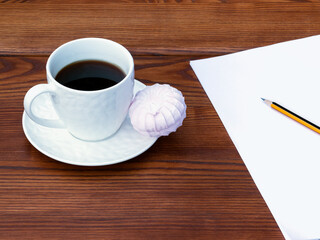 White cup of coffee, pink zefir and empty A4 paper on the wooden background. Traditional russian sweets like marshmallow. Copy space.
