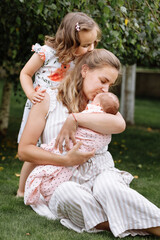 portrait of loving mother and two adorable kids. little girl and newborn baby girl with mom outdoors on summer day. Happy family spent time together in the park