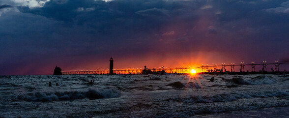 The sun sets below storm clouds behind the lighthouse and catwalk at Grand Haven, Michigan, as a...