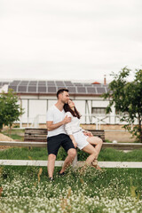 Loving couple is sitting in the summer park on white fence. man and woman are hugging outdoors on warm day