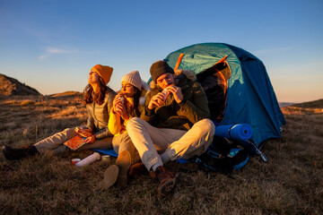 Happy group of friends camping and eating food at the sunset in the mountains. - obrazy, fototapety, plakaty